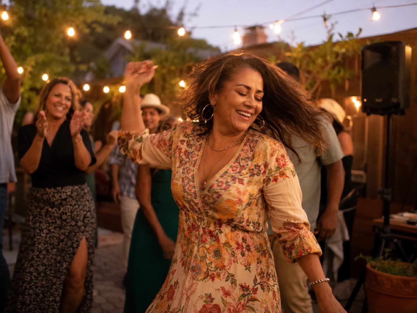 A woman dancing joyfully among friends under warm string lights at an evening garden party.